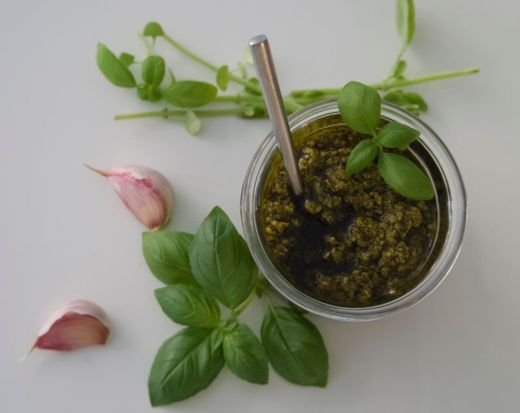 Overhead shot of homemade basil pesto with garlic cloves and fresh basil leaves.