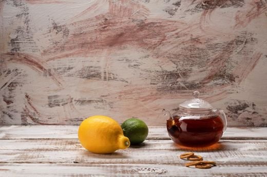 A clear teapot with tea, lemon, and lime on a rustic wooden table.