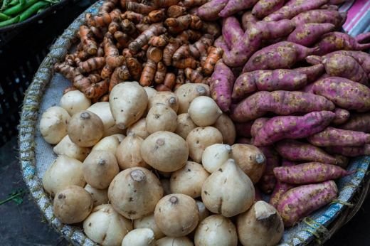 A variety of fresh root vegetables displayed in a traditional market basket in Dhaka, Bangladesh.