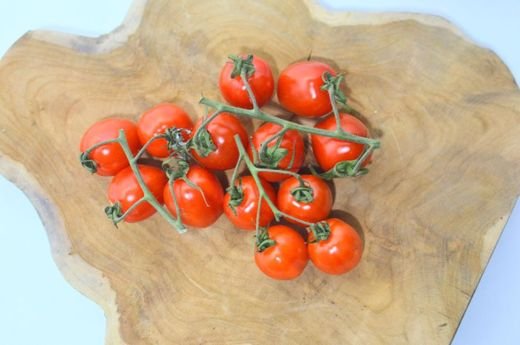 Top view of fresh red cherry tomatoes on green branch placed on shaped wooden board in light room during ripening season