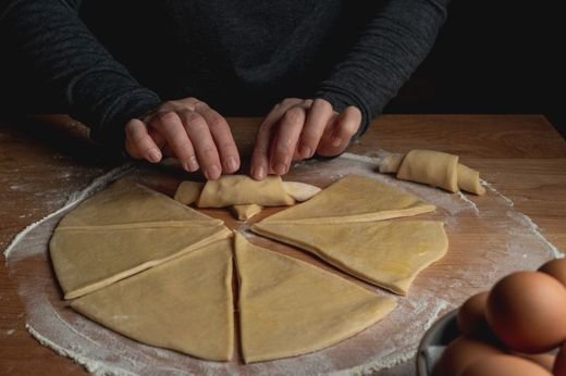 Close-up of hands rolling dough into croissants on a floured surface.